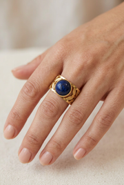 Close-up of a model’s hand wearing the gold leaf ring with a deep-blue stone