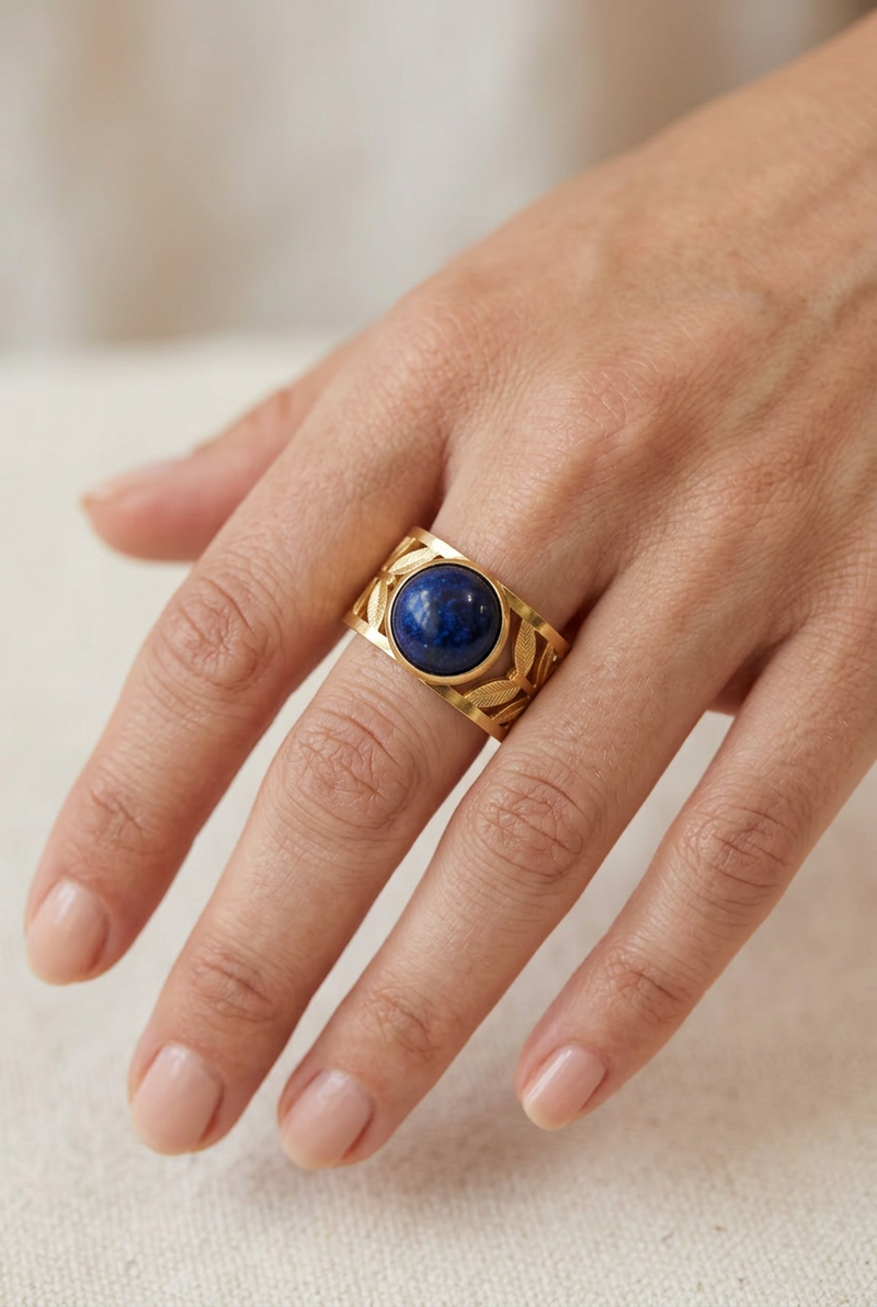 Close-up of a model’s hand wearing the gold leaf ring with a deep-blue stone