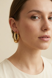 Young adult model wearing the sculptural gold hoop earrings