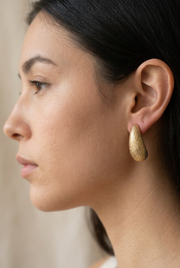 Young adult model wearing the textured gold earrings in close-up