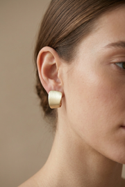 Young adult model wearing the textured pale gold earring in a tight daylight close-up