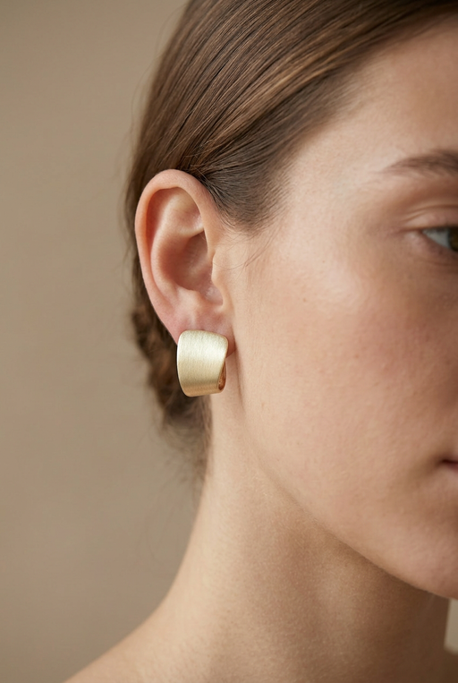 Young adult model wearing the textured pale gold earring in a tight daylight close-up