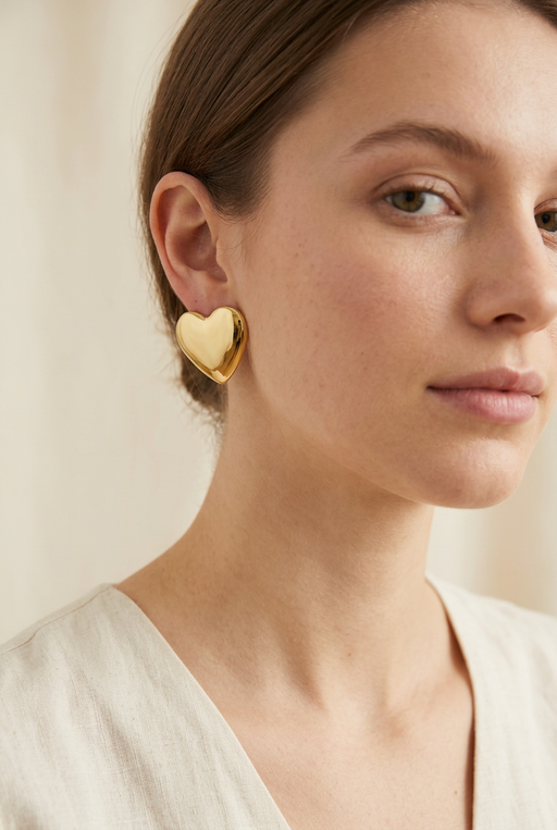 Younger adult model wearing the gold heart earrings